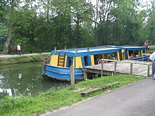 Barge General Harrison of Piqua on the canal in the Piqua, Ohio, Historical Area, in July 2006. Note the captain steering the canal boat and the towing mule  on the towpath on the far side. The canal is wide enough to permit two barges to pass.