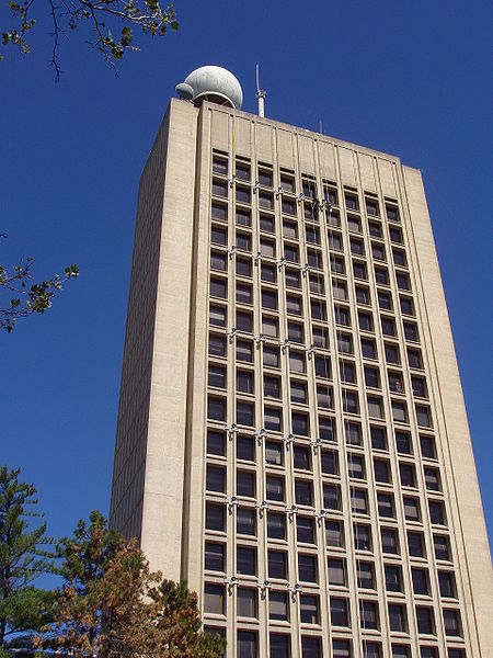 The Green Building from the ground. It is a tall concrete building with many square windows. On the roof is a white sphere and what looks like a tall antenna.