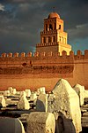 Un cuadro con una docena de tumbas de piedra, todas encerradas dentro de un gran muro.  Una gran torre se encuentra detrás del muro de varios pisos de altura.