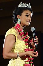 Davuluri speaking, wearing her Miss America tiara, large earrings and a long necklace of red flowers