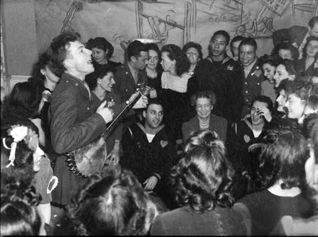 Pete Seeger entertaining Eleanor Roosevelt, honored guest at a racially integrated Valentine's Day party marking the opening of a canteen for the Unit