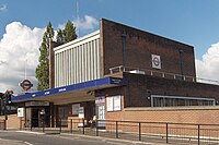 A red-bricked building with a rectangular, dark blue sign reading "WEST ACTON STATION" in white letters all under a blue sky with white clouds