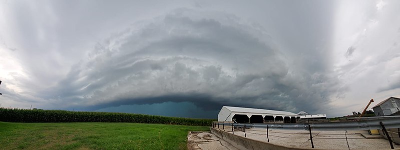 Eine ländliche Skyline mit einer imposanten bogenförmigen Wolke, die den größten Teil des Horizonts bedeckt und dunkelgrau gefärbt ist, aber hellere und dunklere Bereiche aufweist.