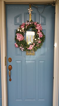 A Christmas wreath adorning a home, with the top left hand corner of the front door chalked for Epiphanytide and the wreath hanger bearing a placard of the Angel Gabriel Christmas wreath.jpg