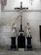 Photographie en couleurs d'une statue du Christ en croix encadré par deux autres statues, une femme et un homme.