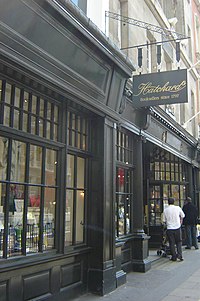 書店ハッチャーズの正面入口をやや斜めに撮影。黒い木を中心にした格子窓の奥にショウウィンドーがあり、白い服を着た男性が奥でこれを覗いている