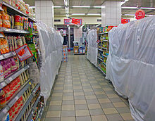 Um corredor estreito de supermercado, sob iluminação fluorescente, com seções bloqueadas por plástico branco