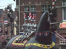 Foto av en karnevaltog som viser en kjempe fra nord: kjempen er en hest og fire ungdommer i rustning, sverd reist, ligger på denne prosesjonsfiguren