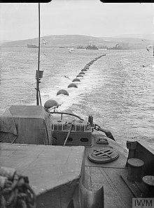 A boom defence is towed across the water by a ship