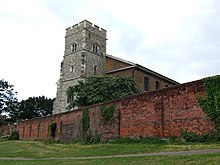 Une tour en pierre grise s'élève au-dessus d'un ancien mur d'enceinte en brique rouge