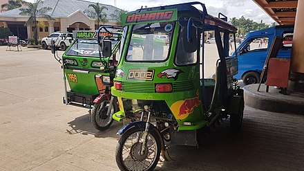 A motorela (right) and a tricycle (left). Note the motorela's centered cab, the sideways passenger seating, and the four wheels.