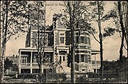 Monochrome photograph of a brick-clad residence featuring numerous architectural elements, including a turret imitating a castle.