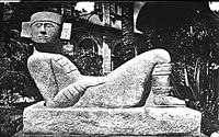 Black and white photograph of a stone carving of a human figure lying down with its knees bent and head turned