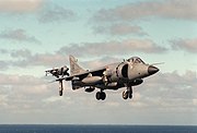 Grey jet aircraft with black radome and large engine inlet hovering with undercarriage extended