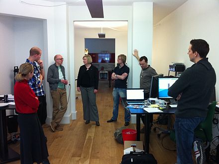 A daily scrum in the computing room. This centralized location helps the team start on time.