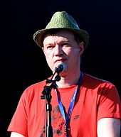 Pas foto berwarna Edwyn Collins, yang berbicara ke dalam mikrofon dan mengintip langsung ke kiri dari mikrofon.