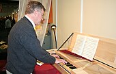 Photographie d’un homme s’appuyant sur un instrument de musique.