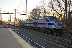 A MARC Penn Line train pulls out of Odenton station while a Northeast Regional train pulled by an AEM-7 passes through.