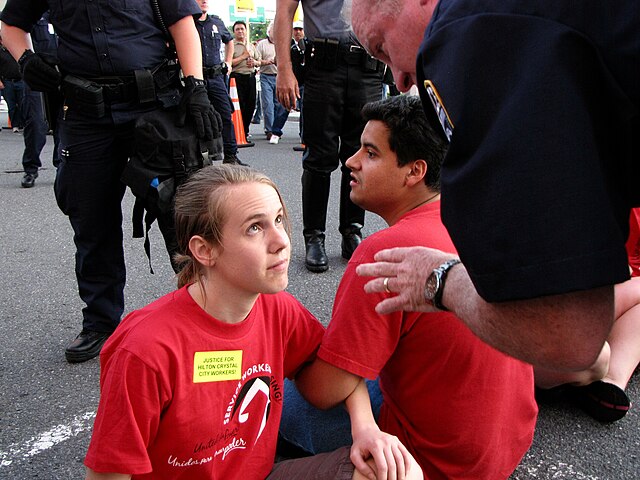 A police officer speaks with a demonstrator at a union picket, explaining that she will be arrested if she does not leave the street. The demonstrator