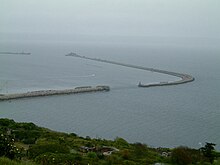 View northeast across Balaclava Bay from the Isle of Portland towards the southern and eastern entrances of Portland Harbour. The dark colour of the water between the two breakwaters is the position a scuttled battleship, HMS Hood.