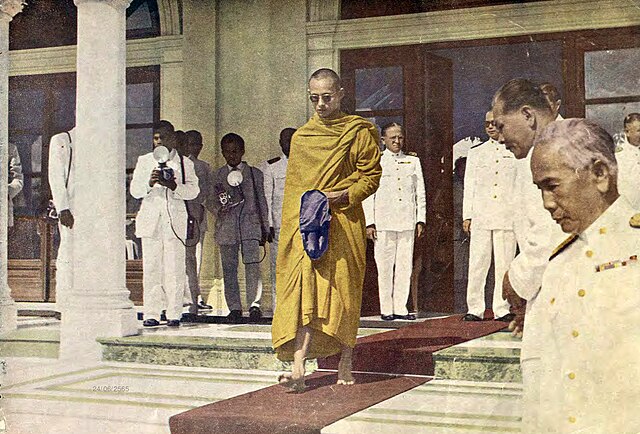 On 31 October 1956, the monk Bhumibalo visited the Government House to ask for alms. Prime Minister Plaek Phibunsongkhram is on the right.