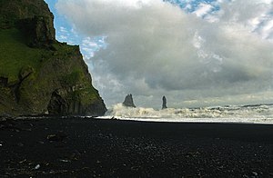 Plaża Reynisfjara, z lewej widoczne zbocze klifowe Reynisfjall z widocznym wejściem do groty Hálsanefshellir. Z morza sterczą bazaltowe kolumny Reynisdrangar (Statek Trolli)