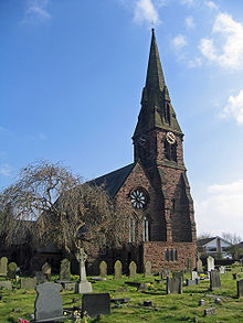 Church facade with a rose window and the steep roof of a Gothic style church.  There are gravestones in the foreground, a leafless tree stands on the left.