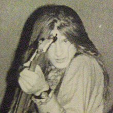 Young man with shoulder length hair holding a bass guitar and smiling