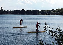 Due bagnini del DLRG tedesco pattugliano un'area balneare pubblica di un lago su stand-up paddle a Monaco di Baviera