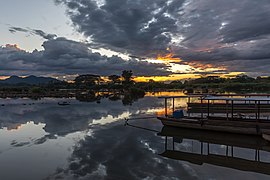 Réflexion dans l'eau d'un coucher de soleil avec des nuages gris et orange au-dessus du Mékong, et deux pirogues amarrées à la berge à Don Det. Novembre 2019.