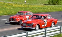 A Saab 93 (left) and a Volvo Amazon (right) line up to race.