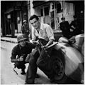 American officer and French partisan crouch behind an auto during a street fight in a French city