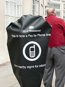 A closed (hooded / out of use) parking meter and a man paying for his parking by telephone. Seen in the Westminster area of London. Closed Parking Meter - Man Paying By Phone.JPG