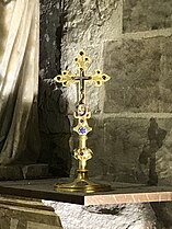 Petite croix dorée contenant, en son centre, visible par une ouverture vitrée, des éclats de bois.