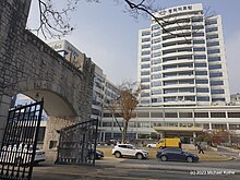 Das Bild zeigt ein weißes Hochhaus und ein Steintor mit geöffneten Türen