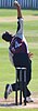 A man with dark hair and a burgundy, grey and black cricket uniform with 'Gregory 24' visible on the back is bowling a white cricket ball.