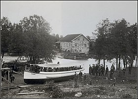 Omtrent 70 medlemmer af Teknologföreningen i Borås [1] på rejse med Svanen i året 1892. 
 Damperen er på vej op ud af Visken for at gøre et sving omkring vandfaldet ved Ålgården og derpå fortsætte sin vandrejse til Öresjö. 
 I forenden står konstruktøren selv, Carl Jacob Magnell.