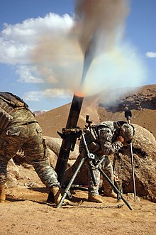 United States Army soldiers firing an M120 mortar (round visible in smoke) during the War in Afghanistan M120 Mortar in Zabol Province, Afghanistan.jpg