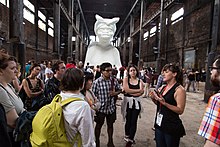 Visitors at Walker's A Subtlety. The white sculpture depicting a woman in the shape of a sphinx is visible in the background. New York Arts Practicum, A Subtlety.jpg