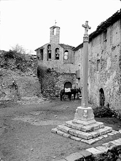 Plaça de Pilzán amb una creu de Terme i dos cavalls, al fons un campanar.jpeg