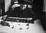 A Wren organizing game materials. The wooden pieces represent escort ships, the black board with white shapes represents a convoy, the wire wool represents smoke.