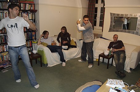 A typical gaming scene in the December 2006. People hang out while two gamers play a Nintendo Wii with motion controls.