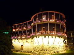 Maison à balcon de bois illuminée, construite sur les remparts de la vieille ville.