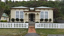 Ein Haus im edwardianischen Stil mit einem weißen Zaun und Wald im Hintergrund