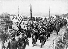 Gambar dari Pasukan Ekspedisi Amerika berbaris melintasi jembatan kecil memegang bendera di Perancis
