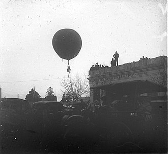 An early hot air balloon flight in 1904 watched by pedestrians with vehicles at Tres Cruces. C11f108.Globo aerostatico en Tres Cruces.jpg