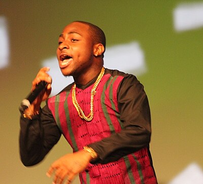 Man wearing red shirt and gold chain performing with microphone in hand