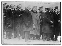 Photographie noir et blanc d'un groupe d'homme, la plupart en civil, certains hommes portent un manteau militaire.