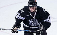 Ein junger männlicher Eishockeyspieler in voller Ausrüstung, einschließlich einer Gesichtsmaske, läuft mit einem entschlossenen Ausdruck auf die Kamera zu, während er an der Kamera vorbeischaut.