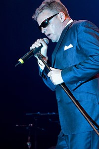 Suggs (pictured in 2008) and his band Madness had four singles in the UK top 10 in 1982, including their only number-one hit, "House of Fun". Madness (band) 2008.06.20 005.jpg